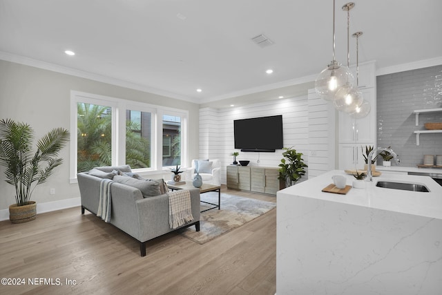 living room featuring sink, light wood-type flooring, and crown molding