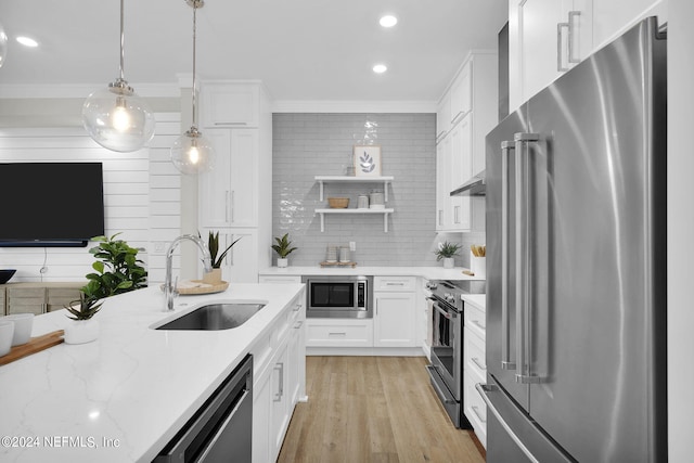 kitchen featuring premium appliances, pendant lighting, sink, white cabinets, and light stone counters