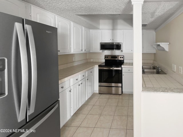 kitchen featuring appliances with stainless steel finishes, decorative columns, white cabinetry, sink, and light tile patterned floors