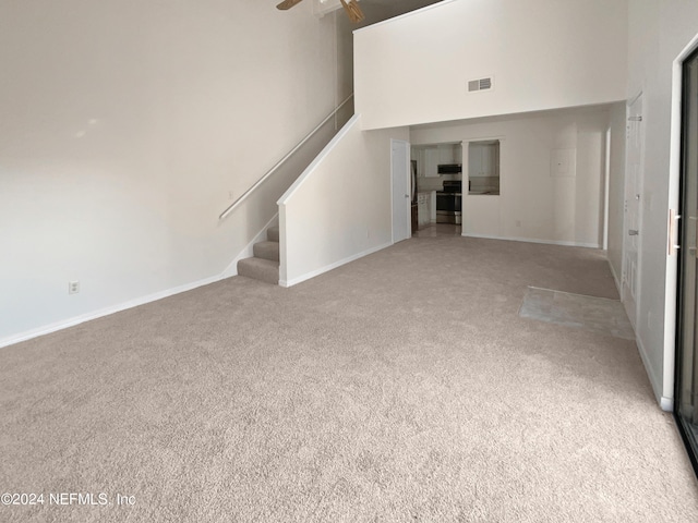 unfurnished living room with carpet flooring, ceiling fan, and a towering ceiling