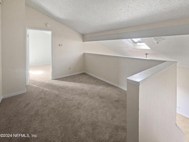 additional living space featuring light colored carpet, lofted ceiling with skylight, and a textured ceiling