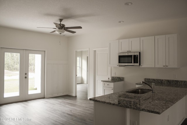 kitchen featuring kitchen peninsula, sink, white cabinetry, dark stone counters, and light hardwood / wood-style floors