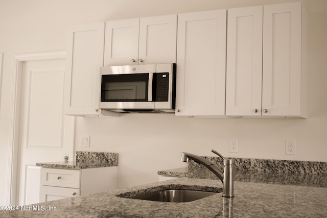 kitchen with light stone countertops, sink, and white cabinetry