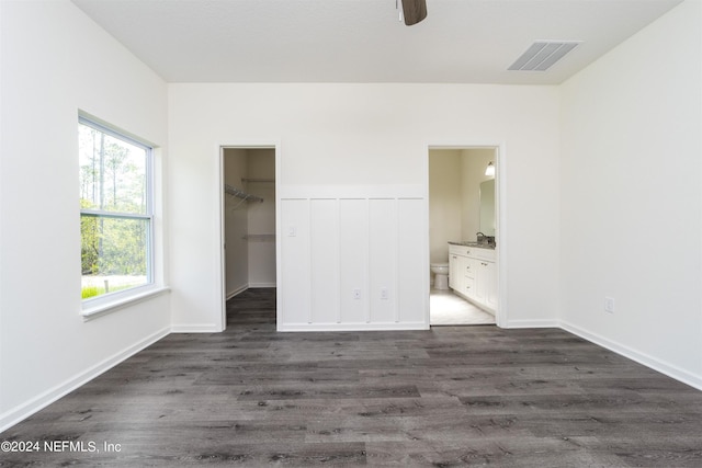 unfurnished bedroom with ceiling fan, ensuite bathroom, dark hardwood / wood-style flooring, a spacious closet, and a closet