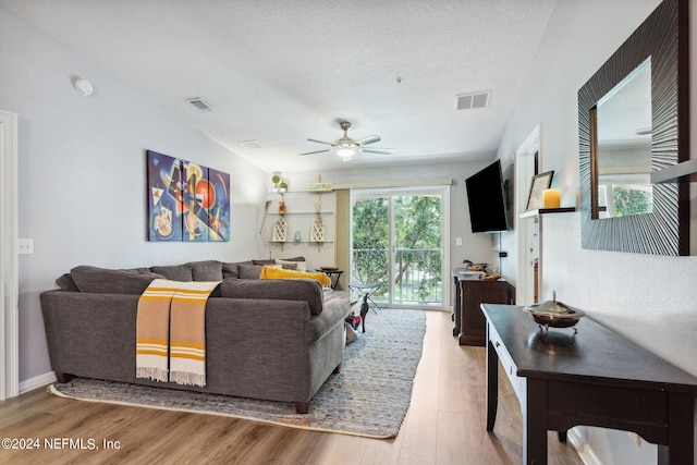 living room with light hardwood / wood-style floors, a textured ceiling, and ceiling fan