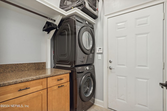 clothes washing area featuring light tile patterned floors, stacked washer and clothes dryer, and cabinets