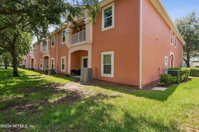 rear view of property with a balcony, a yard, and central AC