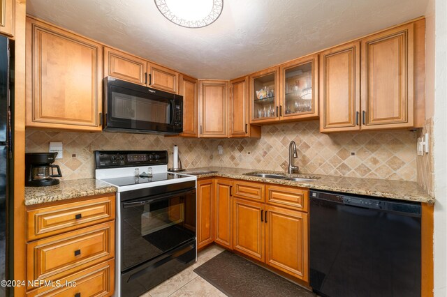 kitchen with light tile patterned floors, black appliances, light stone countertops, decorative backsplash, and sink