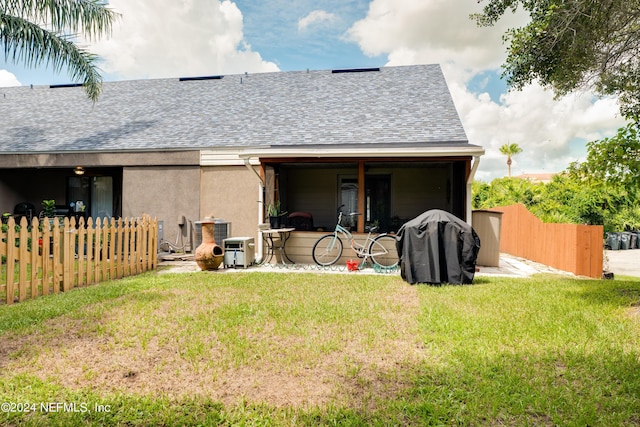 rear view of house with a shingled roof, stucco siding, a yard, and fence