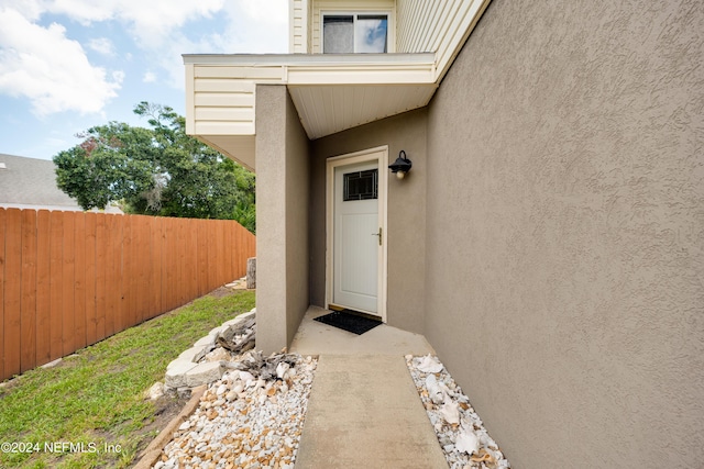 view of exterior entry featuring fence and stucco siding