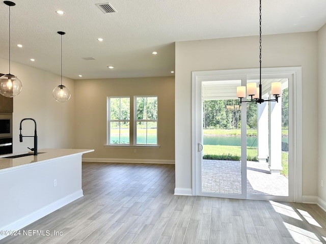 kitchen featuring sink, light wood-type flooring, hanging light fixtures, stainless steel oven, and a textured ceiling