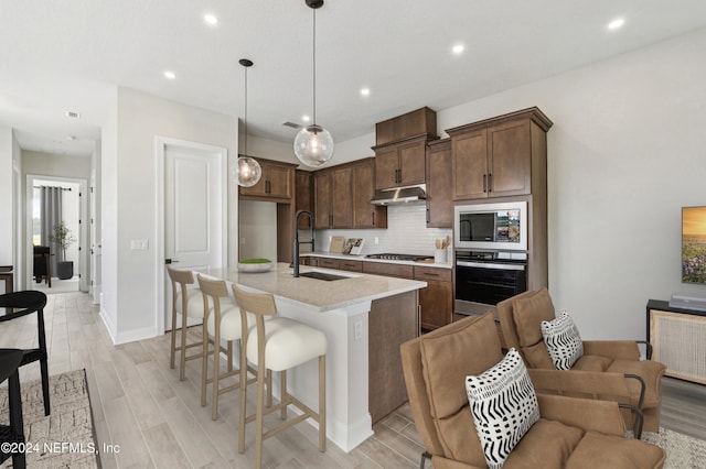 kitchen featuring sink, appliances with stainless steel finishes, a kitchen island with sink, hanging light fixtures, and decorative backsplash