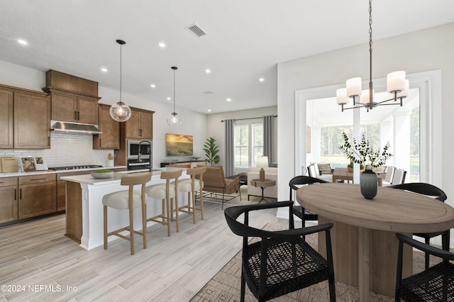 kitchen with a kitchen island with sink, pendant lighting, light wood-type flooring, and decorative backsplash