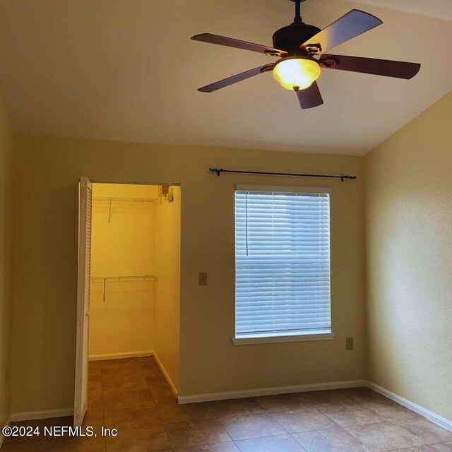 tiled empty room with ceiling fan, a wealth of natural light, and vaulted ceiling