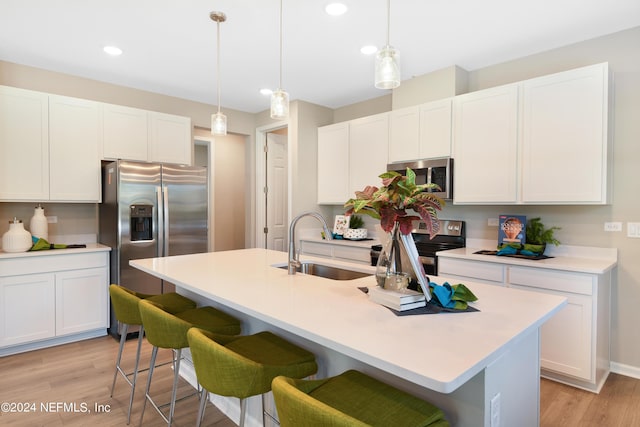 kitchen with white cabinetry, stainless steel appliances, a center island with sink, and hanging light fixtures