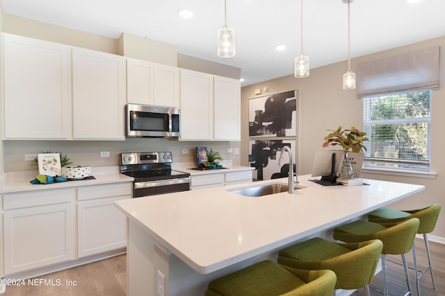 kitchen featuring a center island with sink, sink, hanging light fixtures, stainless steel appliances, and white cabinets