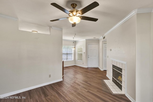 unfurnished living room with a tiled fireplace, dark wood-type flooring, crown molding, and ceiling fan