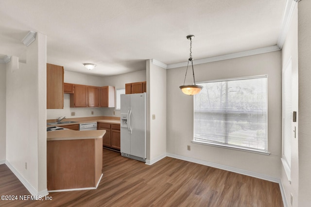 kitchen featuring white appliances, kitchen peninsula, hanging light fixtures, hardwood / wood-style flooring, and ornamental molding