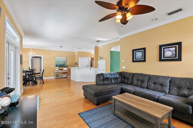 living room featuring light wood-type flooring, ceiling fan with notable chandelier, ornamental molding, and a textured ceiling