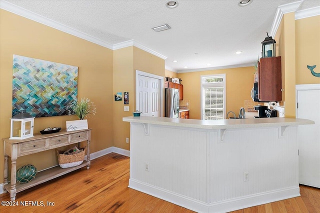 kitchen with crown molding, a breakfast bar area, appliances with stainless steel finishes, light hardwood / wood-style flooring, and a textured ceiling