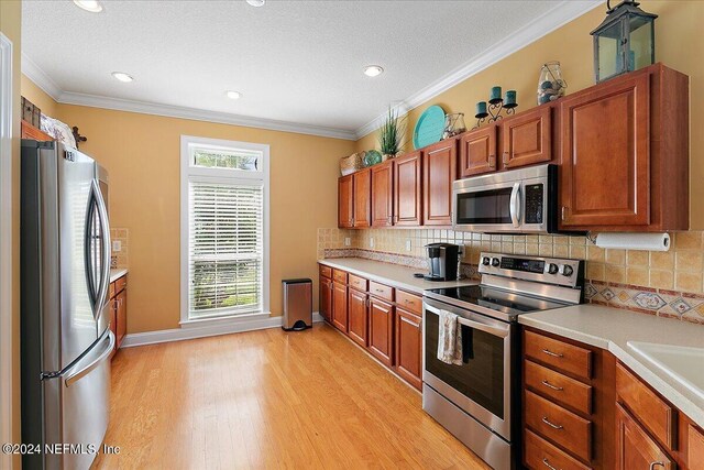 kitchen featuring light hardwood / wood-style floors, appliances with stainless steel finishes, decorative backsplash, and crown molding