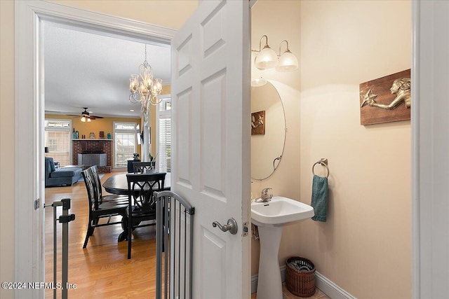 bathroom featuring a brick fireplace, wood-type flooring, and ceiling fan with notable chandelier