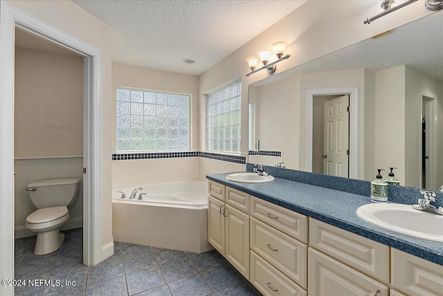 bathroom with double vanity, tiled bath, toilet, and a textured ceiling