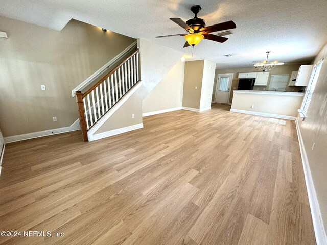 unfurnished living room with ceiling fan with notable chandelier, light wood-type flooring, and a textured ceiling