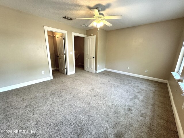 unfurnished bedroom with light carpet, ceiling fan, a walk in closet, and a textured ceiling