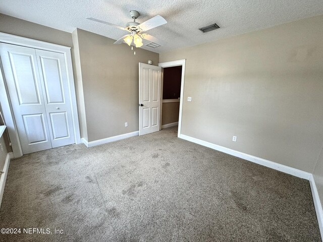 unfurnished bedroom featuring a closet, a textured ceiling, light colored carpet, and ceiling fan