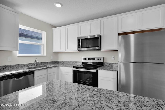 kitchen featuring a textured ceiling, a sink, white cabinetry, appliances with stainless steel finishes, and light stone countertops