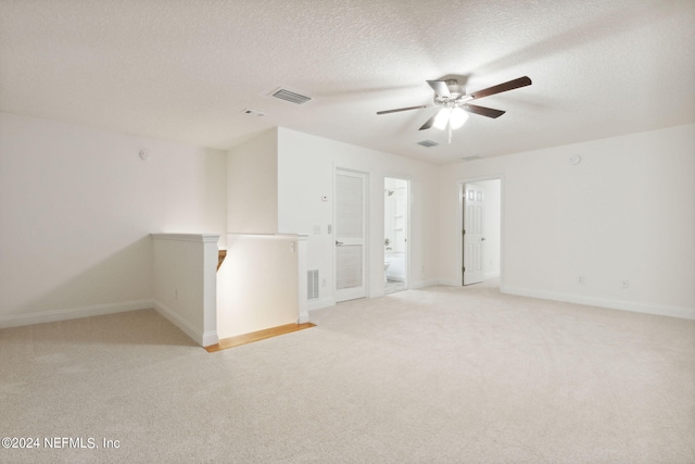 unfurnished room featuring a textured ceiling, ceiling fan, and light colored carpet