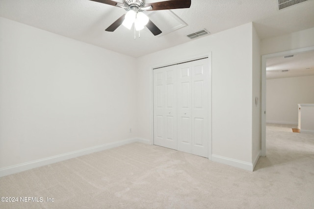 unfurnished bedroom with ceiling fan, light carpet, a closet, and a textured ceiling