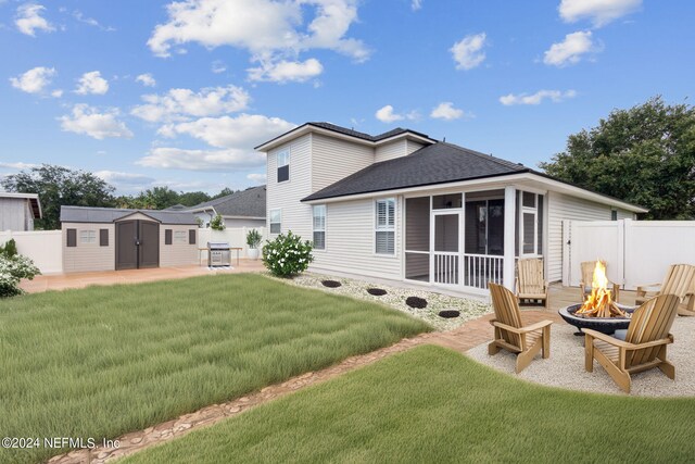 back of house featuring a sunroom, a storage shed, a patio area, an outdoor fire pit, and a lawn