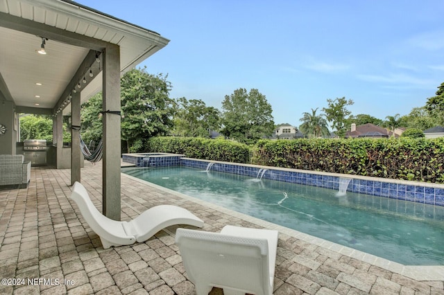 view of pool with a patio, an in ground hot tub, pool water feature, and exterior kitchen