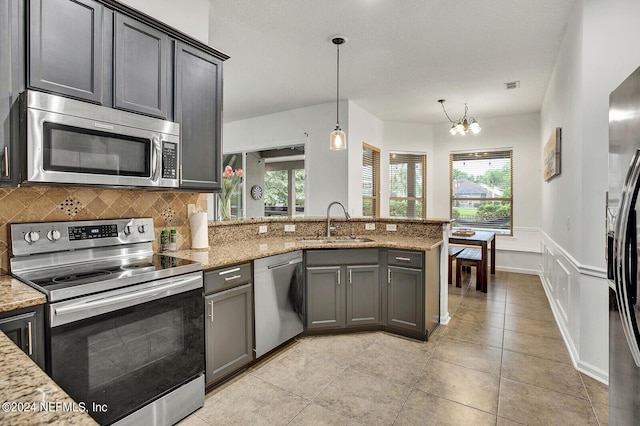 kitchen featuring appliances with stainless steel finishes, sink, hanging light fixtures, light stone counters, and kitchen peninsula