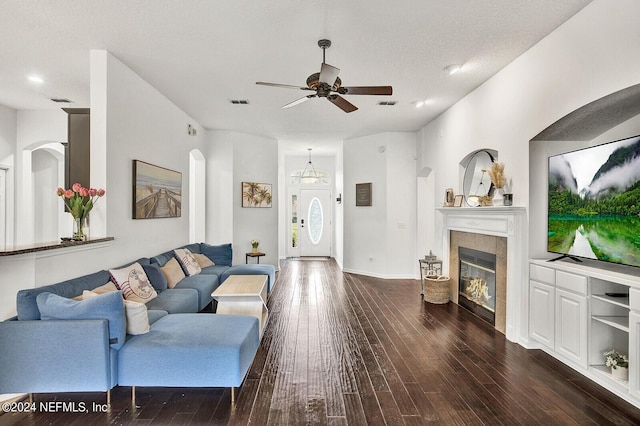 living room featuring a tiled fireplace, ceiling fan, dark wood-type flooring, and a textured ceiling