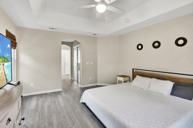 bedroom with a raised ceiling, light wood-type flooring, and ceiling fan