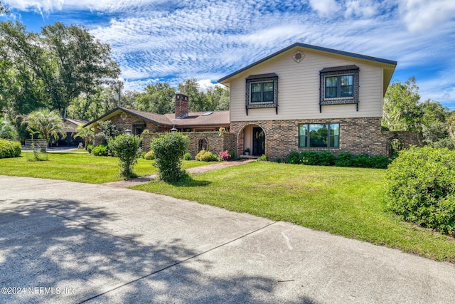 view of front of property featuring a chimney, a front lawn, and brick siding