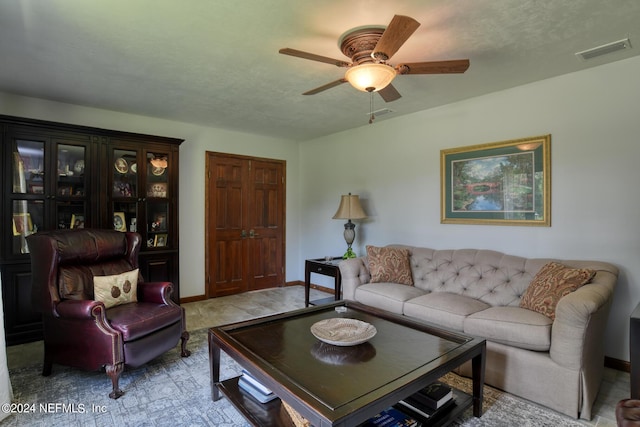 living room with baseboards, ceiling fan, visible vents, and a textured ceiling