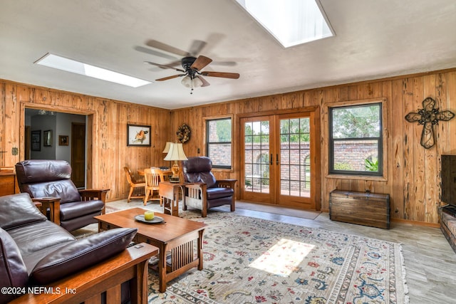 living room featuring a ceiling fan, a skylight, french doors, and wood walls