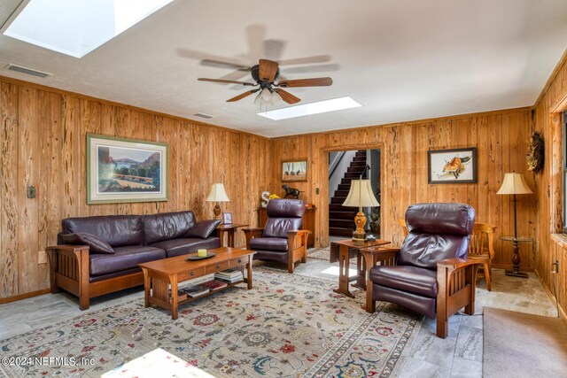 living room with a skylight, ceiling fan, and wood walls