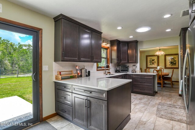 kitchen featuring backsplash, freestanding refrigerator, a sink, dark brown cabinetry, and a peninsula