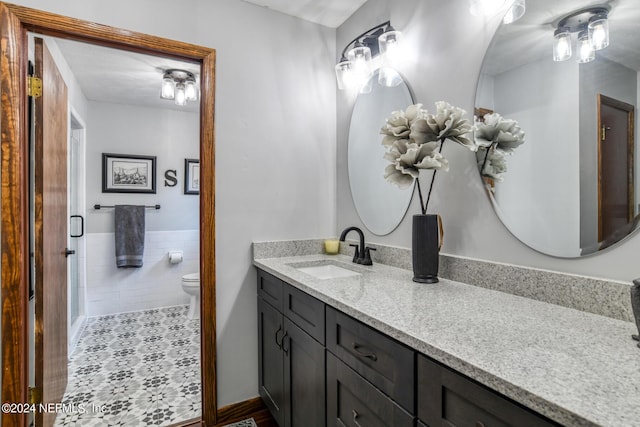 bathroom featuring a wainscoted wall, tile walls, toilet, vanity, and tile patterned flooring