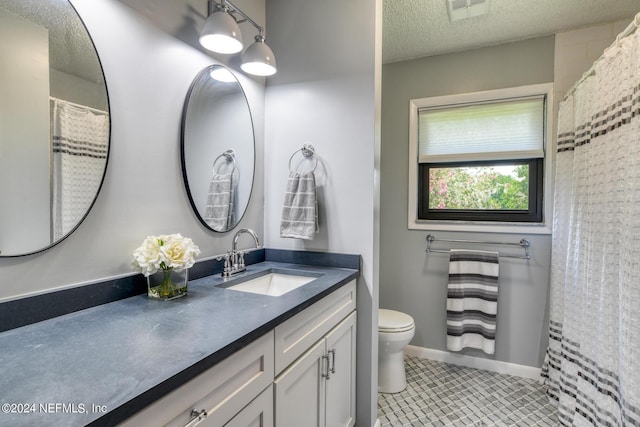 full bath featuring visible vents, toilet, vanity, a textured ceiling, and baseboards