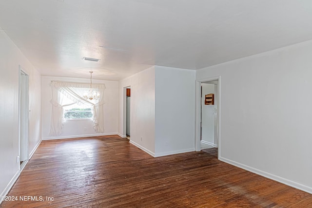 spare room featuring baseboards, wood finished floors, visible vents, and a notable chandelier