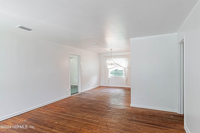 spare room featuring an inviting chandelier, visible vents, baseboards, and wood finished floors