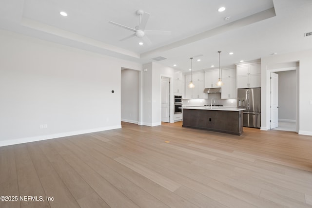 unfurnished living room featuring sink, a tray ceiling, light hardwood / wood-style flooring, and ceiling fan