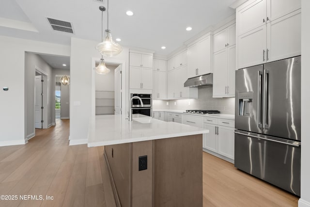 kitchen featuring light hardwood / wood-style flooring, a kitchen island with sink, hanging light fixtures, stainless steel appliances, and white cabinets