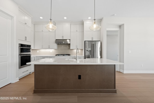 kitchen with white cabinetry, hanging light fixtures, a kitchen island with sink, and stainless steel appliances